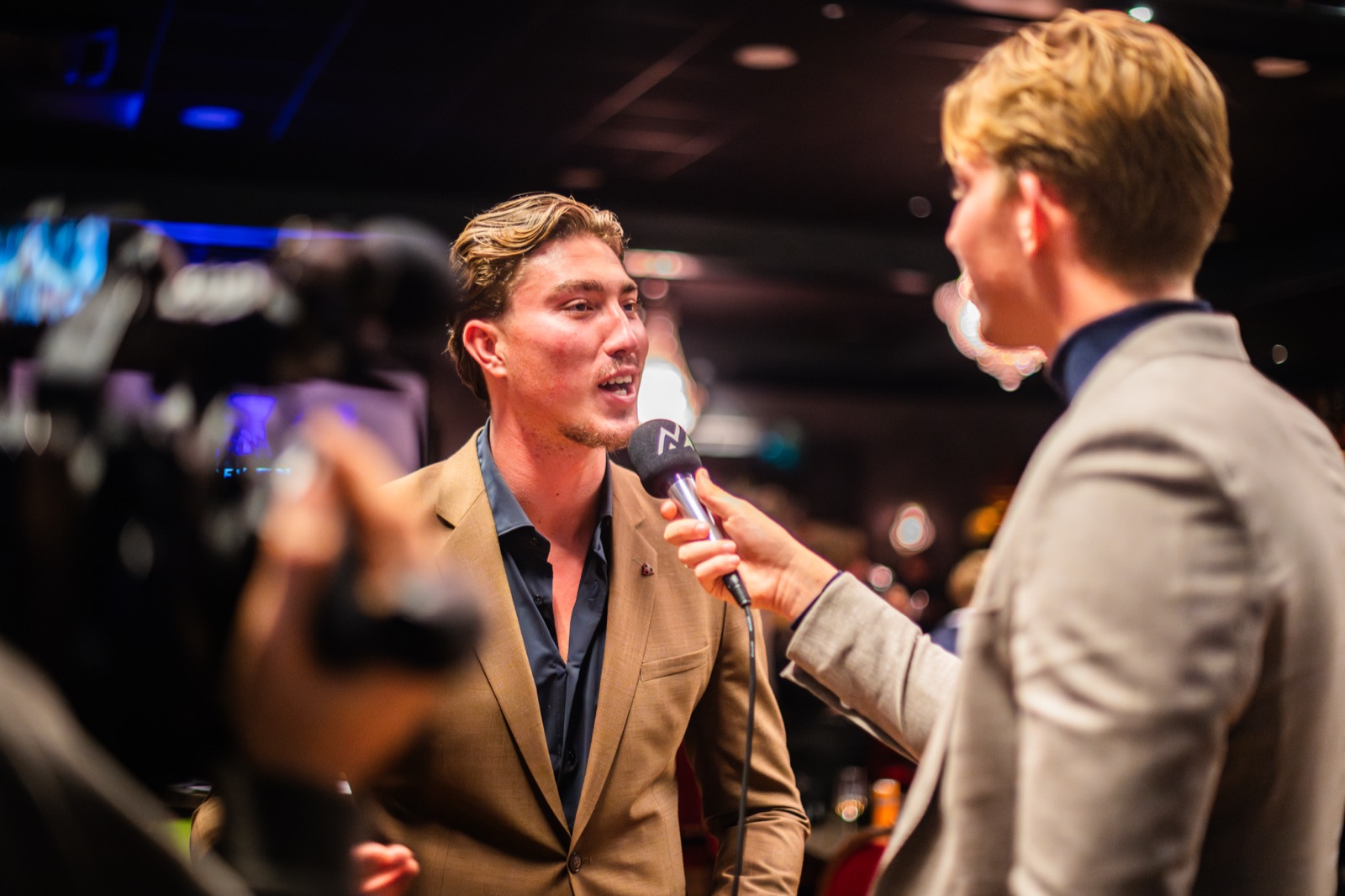 Daan interviewt een gast met microfoon, camera filmt mee